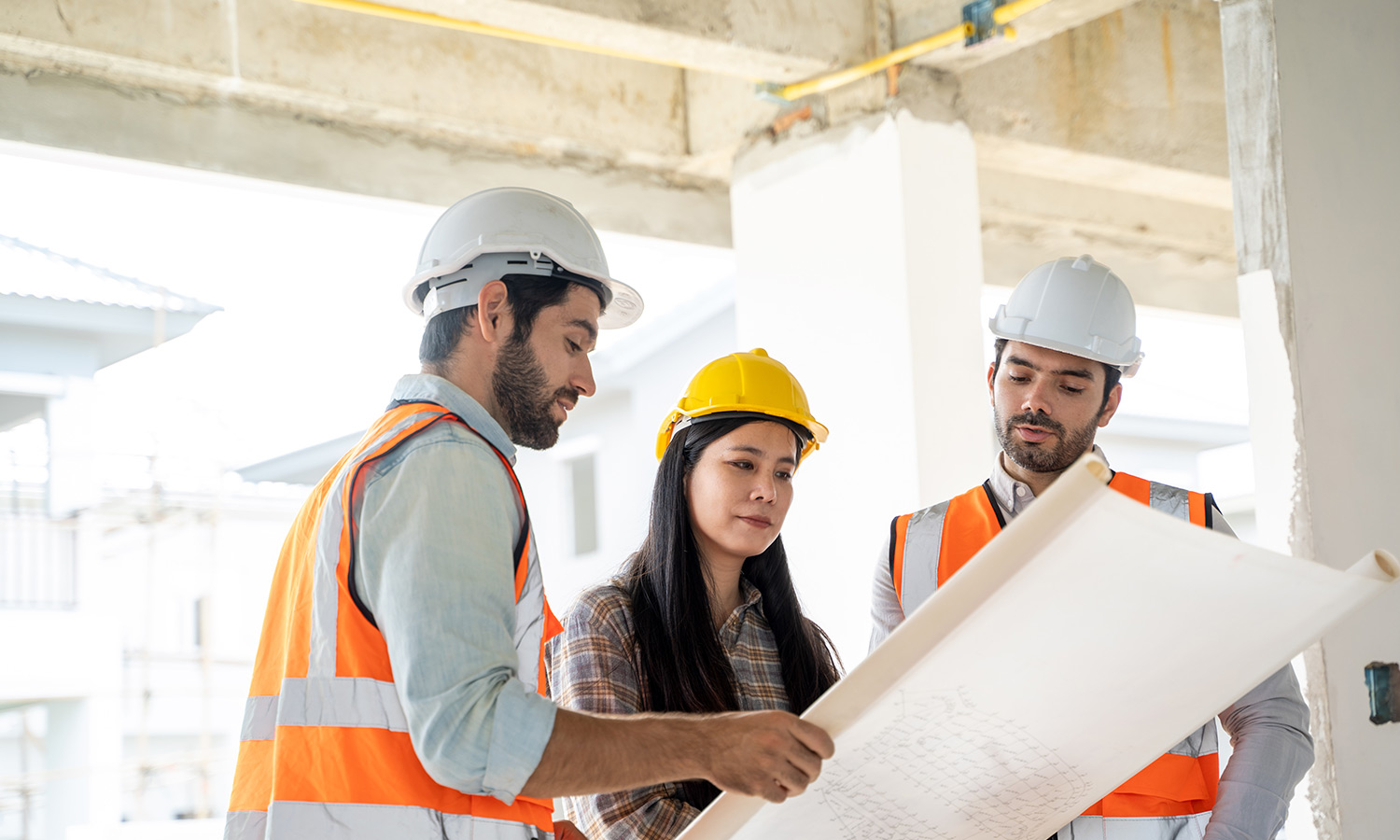 Two male contractors and female client assessing blueprints on building site